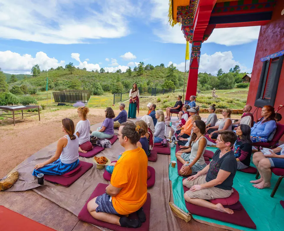 Practitioners meditate on cushions on the temple porch during an outdoor teaching