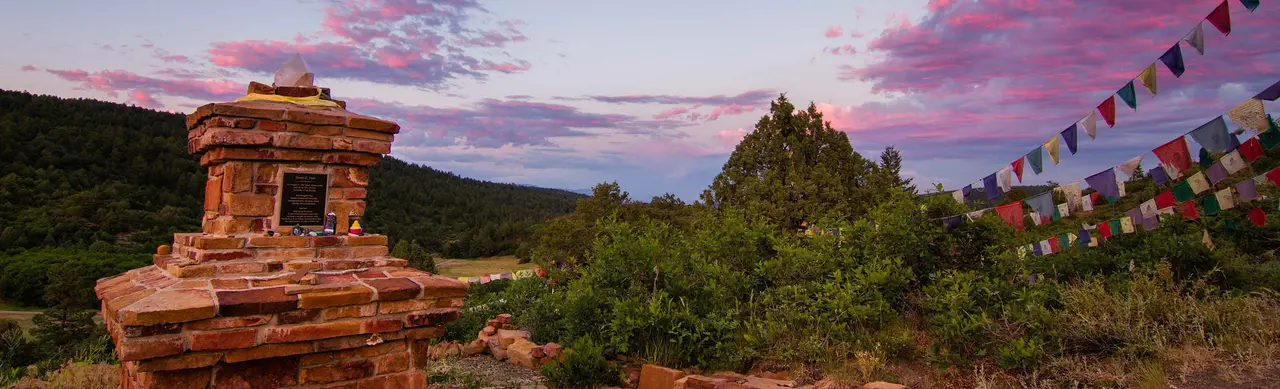 A red sandstone memorial stupa beside strings of prayer flags at dusk